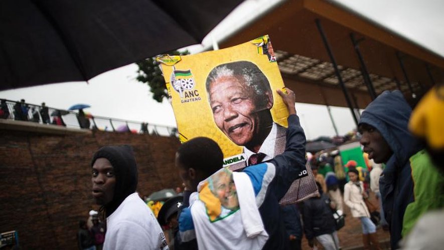 Des Sud-Africains tiennent un poster de Nelson Mandela, au stade de Soweto après la cérémonie d'hommage, le 10 décembre 2013