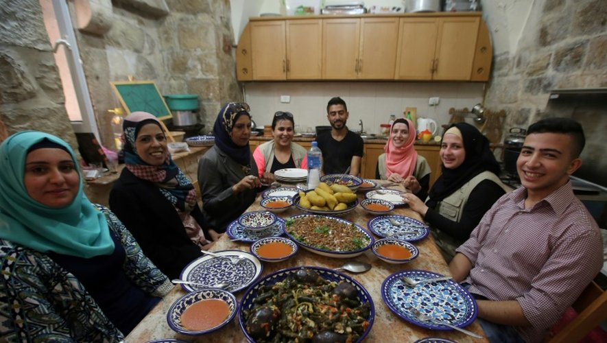 Des Palestiniennes et des étrangers assis à table devant des spécialités palestiniennes préparées lors d'un cours de cuisine à la maison de Fatima Kadumy (3e g), le 19 septembre 2015 à Naplouse