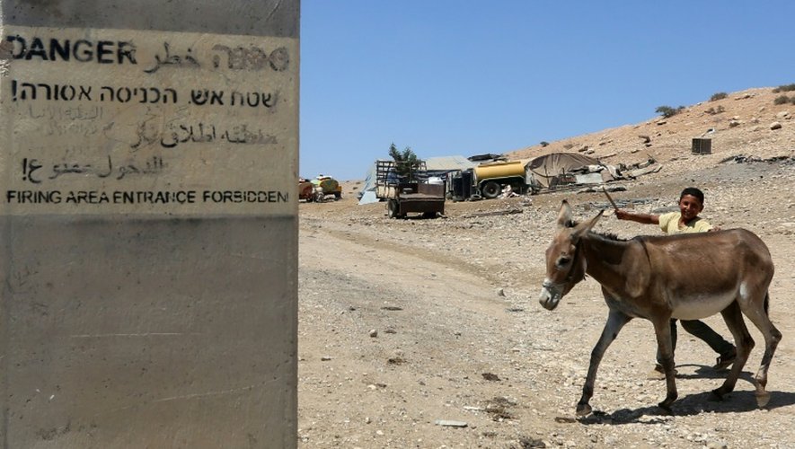 Un Palestinien avec son âne traverse une route dans la région de Toubas (Vallée du Jourdain), où une pancarte prévient que la zone est une zone de tirs, le 19 juillet 2016