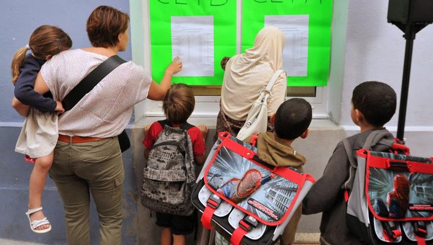 Des parents et leurs enfants devant un tableau d'affichage d'une école primaire