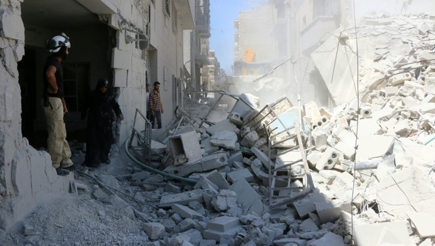 Des Syriens devant les ruines d'un immeuble détruit par un raid aérien le 14 juillet 2016 à Alep