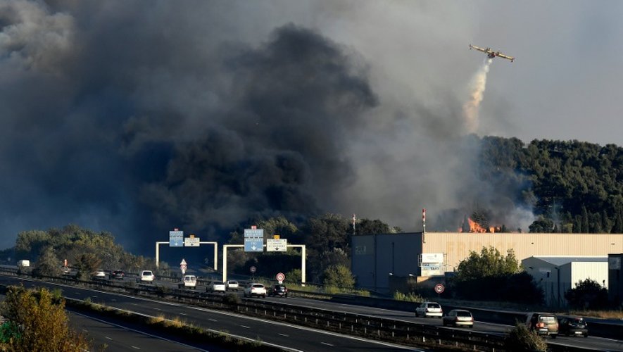 Des automobilistes passent sur l'autoroute près de Vitrolles, dans le sud de la France, où sévit un violent incendie, le 10 août 2016