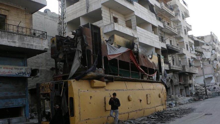 Un rebelle syrien armé devant des immeubles bombardés et des carcasses de bus, le 27 septembre 2014 à Alep, dans le nord de la Syrie