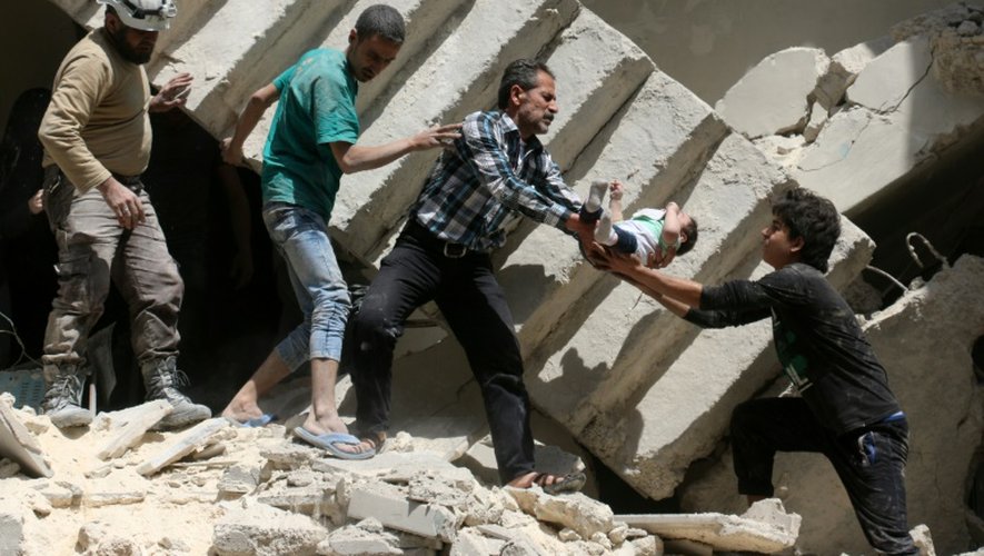 Des volontaires de la Défense civile syrienne, sortent un enfant des décombres d'un immeuble bombardé à Alep le 28 avril 2016