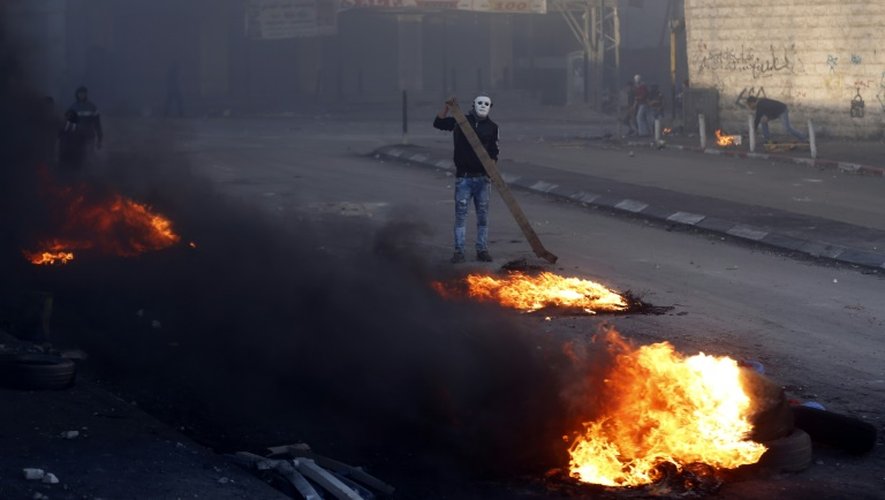 Un Palestinien masqué brûle des pneus lors de heurts avec les forces de sécurité israéliennes, à Chouafat, le 9 octobre 2015 à Jérusalem-Est