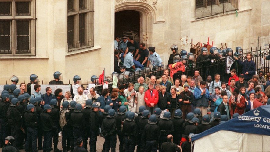 Un gréviste de la faim est sorti sur un brancard de l'église Saint-Bernard, alors qu'un groupe de sympathisants des sans-papiers est encadré par les forces de l'ordre, le 23 août 1996 à Paris