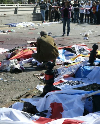 Un proche accroupi près d'un corps  d'une des victimes, recouvertes de drapeaux, du double attentat qui a fait au moins 95 morts à Ankara en Turquie, le 10 octobre 2015