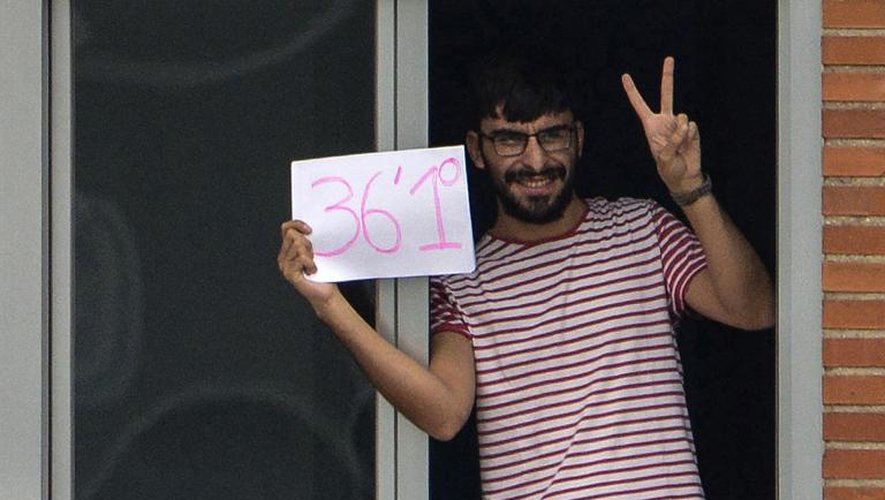 Un homme fait le V de "victoire" en tenant une feuille sur laquelle est écrite sa température à la fenêtre d'une chambre de l'hôpital Carlos III où se trouvent l'aide-soignante espagnole contaminée par le virus Ebola et 15 autres personnes en quarantaine, le 11 octobre 2014 à Madrid
