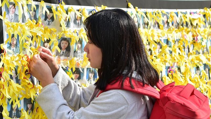 Une jeune femme attache un ruban jaune sur les portraits des victimes du naufrage du ferry sud-coréen Sewol, le 15 octobre 2014 à Séoul