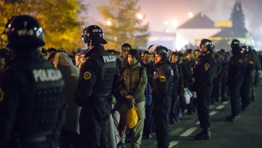 Des policiers slovènes encadrent les migrants sur le point de monter dans un bus le 28 octobre 2015 à Sentilj