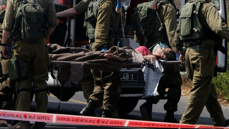 Des soldats Israéliens transportent une civile blessée par un Palestinien lors d'une attaque à la voiture bélier près de la colonie israélienne de Kyriat Arba, en Cisjordanie occupée, le 16 septembre 2016