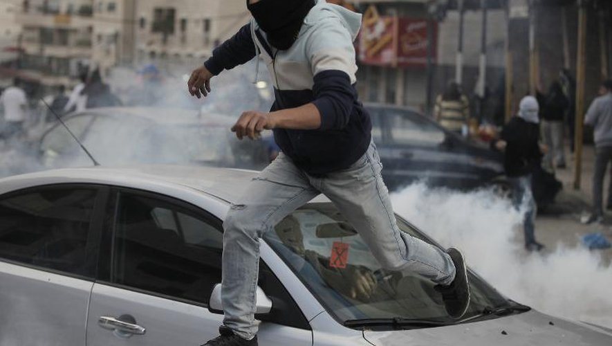 Un jeune Palestinien masqué saute sur une voiture pour échapper aux gaz lacrymogènes lancés par des policiers israéliens, le 5 novembre 2014 au camp de Chouafat, à Jérusalem-Est