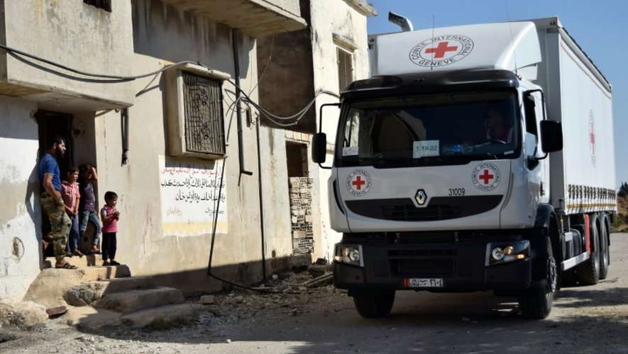 Des Syriens devant chez eux regardent un camion humanitaire du Croissance rouge, au nord de Homs, le 19 septembre 2016