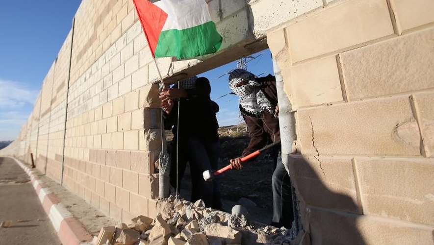 De jeunes Palestiniens brandissent un drapeau palestinien à travers la brèche qu'ils ont creusée dans le mur de séparation entre Israël et le village de Bir Nabala, en Cisjordanie, le 8 novembre 2014