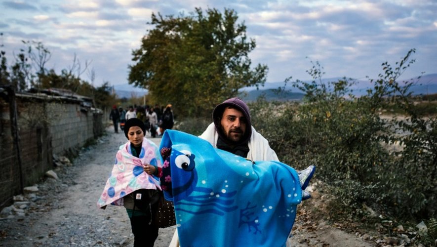 Un homme porte son enfant alors qu'il vient avec d'autres migrants de passer la frontière gréco-macédonienne près de Gevgelija, en Macédoine, le 15 novembre 2015