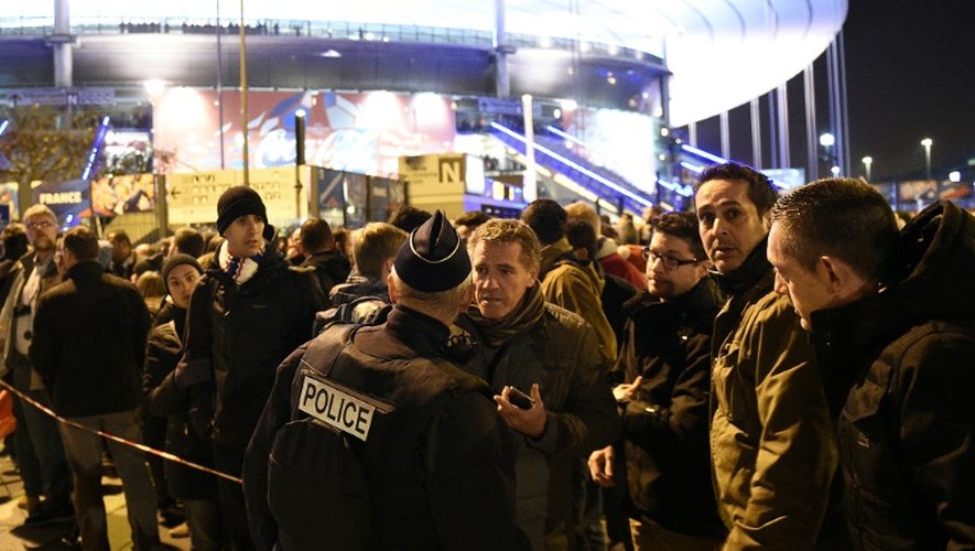 Un policier devant un cordon de sécurité derrière lequel des supporteurs de l'équipe de France de foot attendent après une série d'explosions au Stade de France, le 13 novembre 2015 à Saint-Denis, près de Paris
