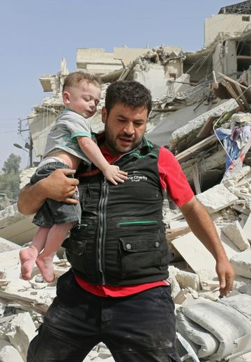 Un syrien porte un enfant hors des ruines après des bombardements qui ont détruit son immeuble dans le quartier de Qatarji au nord d'Alep, le 21 septembre 2016