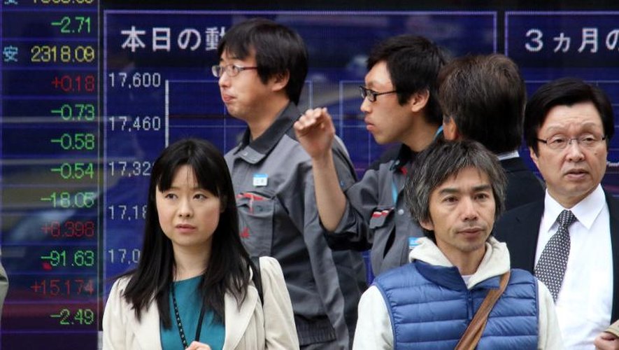 Des piétons japonais passent devant un tableau d'indices boursiers, le 17 novembre 2014 dans une rue de Tokyo