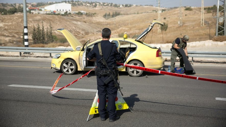 Un policier israélien à côté du taxi d'un chauffeur palestinien qui a tenté de foncer sur des Israéliens avant d'être tué en Cisjordanie, le 22 novembre 2015