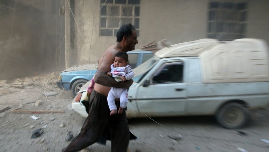 Un homme avec un bébé s'enfuit après des bombardements sur Kafr Batna, dans la banlieue de Damas, le 30 septembre 2016