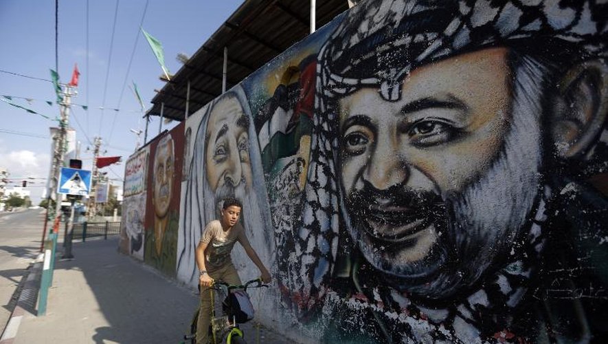 Un Palestinien en vélo passe devant un mur de graffiti représentant (de g à d) le fondateur du FPLP Georges Habache, le leader spirituel du Hamas cheikh Ahmed Yassine et l'ancien leader palestinien Yasser Arafat, le 21 novembre 2014 à Gaza