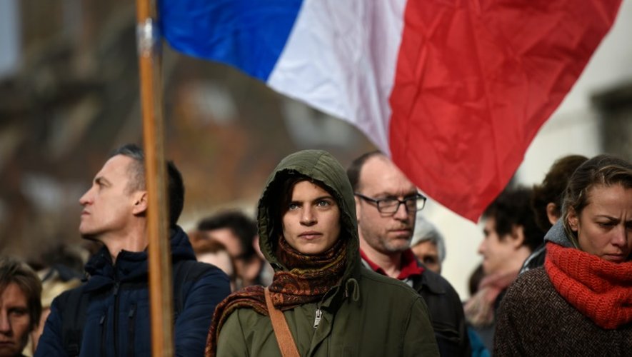 Des passants tiennent le drapeau français le 16 novembre 2015 pendant la minute de silence devant le Carillon, cible des attaques