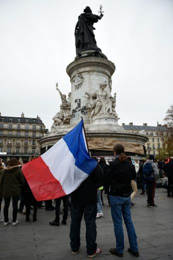 Un homme tenant un drapeau français le 14 novembre 2015 devant la statue place de la République devenue un mémorial aux victimes du 13 novembre