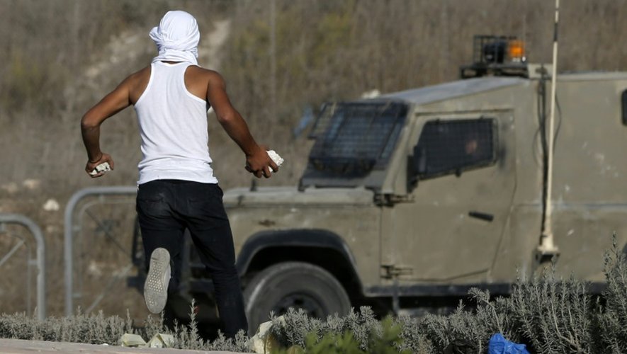 Un Palestinien s'apprête à lancer des pierres en direction d'un véhicule militaire israélien en Cisjordanie près de la ville de al-Ram, nord de Jérusalem le 9 octobre  2016