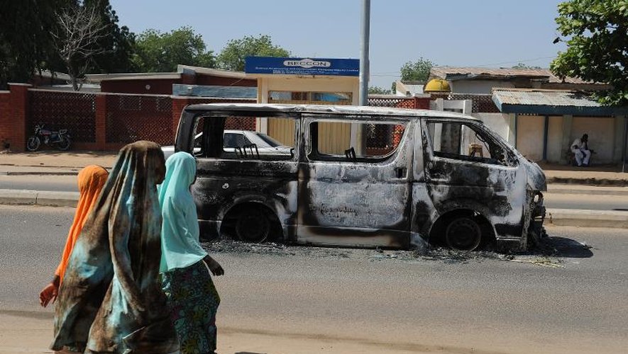 Des habitantes de Damaturu passent devant l'épave d'un véhicule incendié dans une rue de la ville, le 4 novembre 2011 dans le nord-est du Nigeria