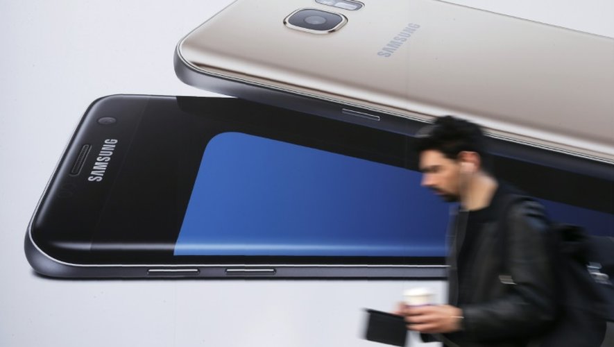 Un homme utilise un smartphone alors qu'il passe devant une publicité pour le Samsung Galaxy S7 à Londres le 11 octobre 2016