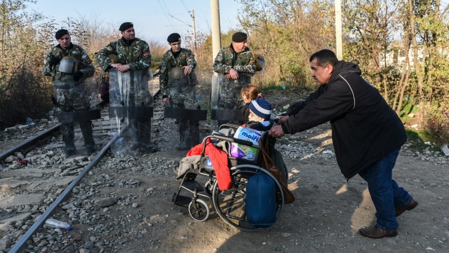 Un homme poussant la chaise roulante d'un migrant traverse la frontière entre la Grèce et la Macédoine près de Gevgelija le 4 décembre 2015
