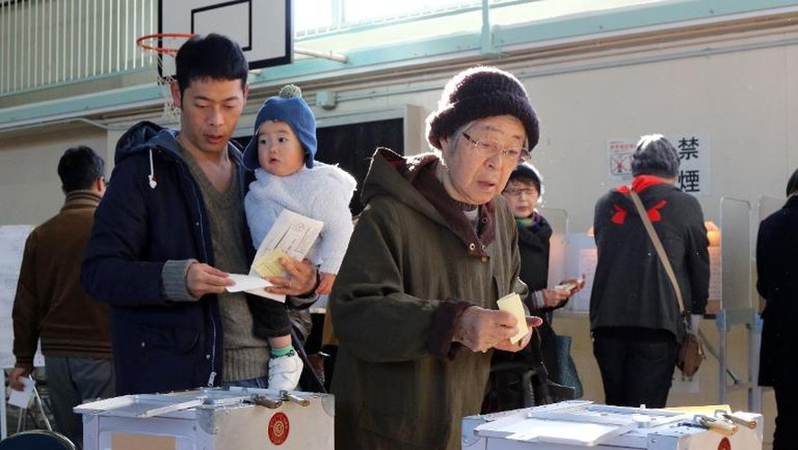 Des Japonais déposent leur bulletin dans l'urne le 14 décembre 2014 à Tokyo