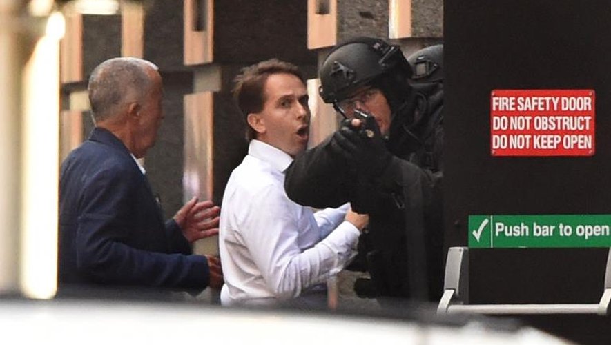 Deux otages (g) ayant réussi à s'enfuir se mettent à couvert derrière un policier (d) durant une prise d'otages dans un café de Sydney, le 15 décembre 2014
