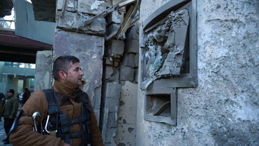 Un officier de sécurité afghan contrôle un des murs criblé de balles après une attaque des talibans dans le quartier diplomatique de Kaboul, le 12 décembre 2015
