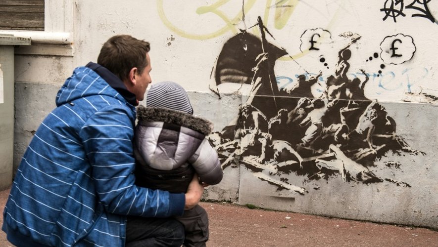 Un homme et un enfant regardent un pastiche de la célèbre toile "Le radeau de la méduse" peint par Banksy sur un mur non loin de la mairie de Calais, le 12 décembre 2015