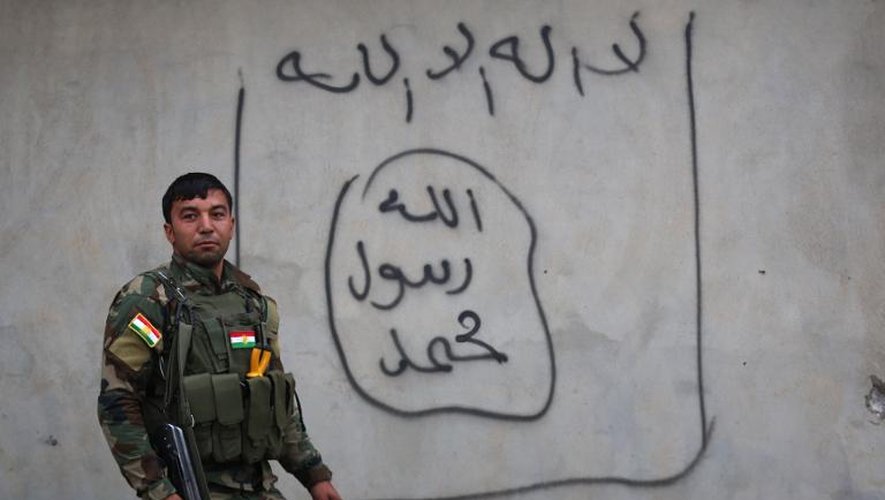 Un combattant Peshmerga pose le 18 décembre 2014 près d'un graffiti du groupe Etat Islamique sur un mur de la ville irakienne de Zummar, près de la frontière avec la Syrie