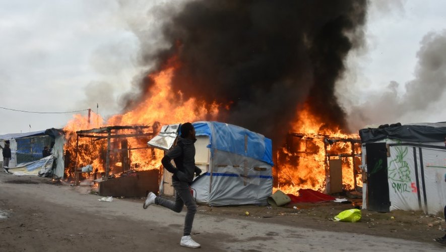 Un migrant court à côté d'un abri en flammes dans le bidonville géant de Calais (nord) en cours d'évacuation le 26 octobre 2016
