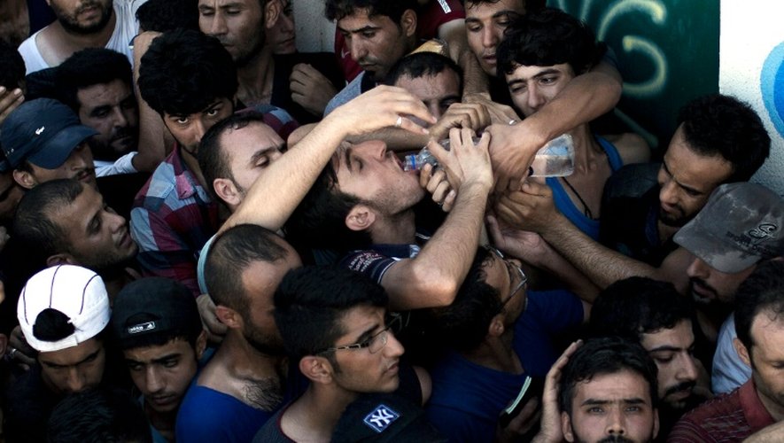 Un migrant boit de l'eau en attendant d'être enregistré par la police dans un stade sur l'île grecque de Kos le 12 août 2015