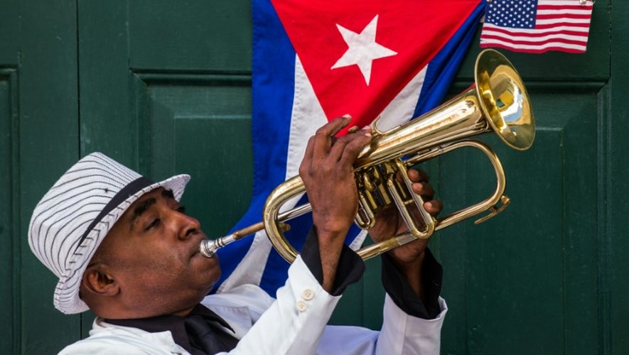 Un homme joue de la trompette devant des drapeaux cubain et américain, à La Havane le 17 décembre 2015