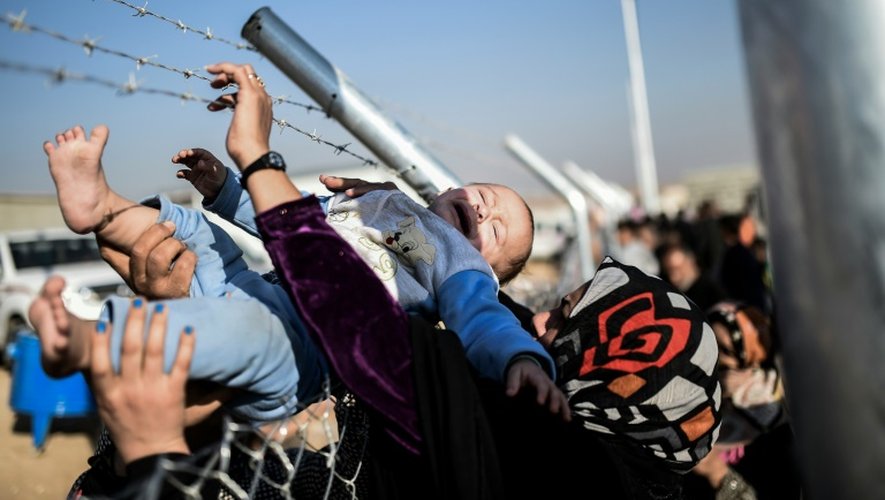 Un bébé est porté au dessus de barbelés pour être récupéré par sa mère dans un camp de réfugiés entre Erbil et Mossoul, le 5 novembre 2016