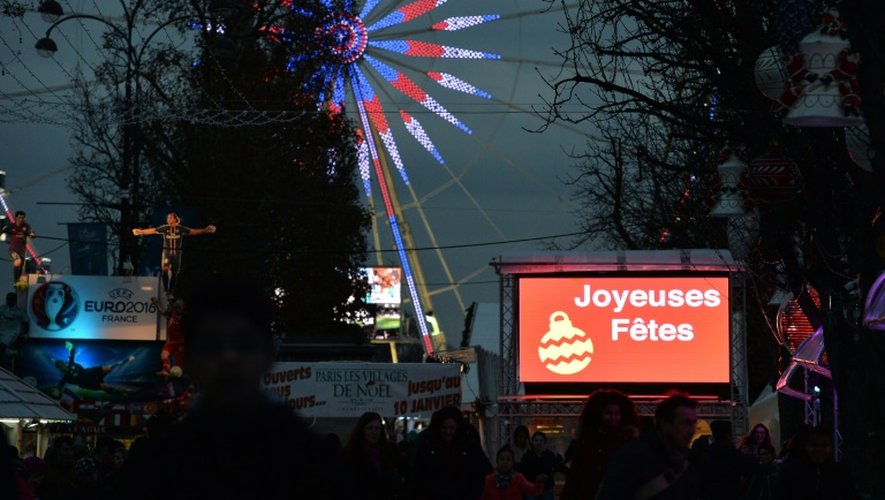 Des personnes se promènent au marché de Noël, près d'un panneau "Joyeuses fêtes" le 24 décembre 2015 à Paris