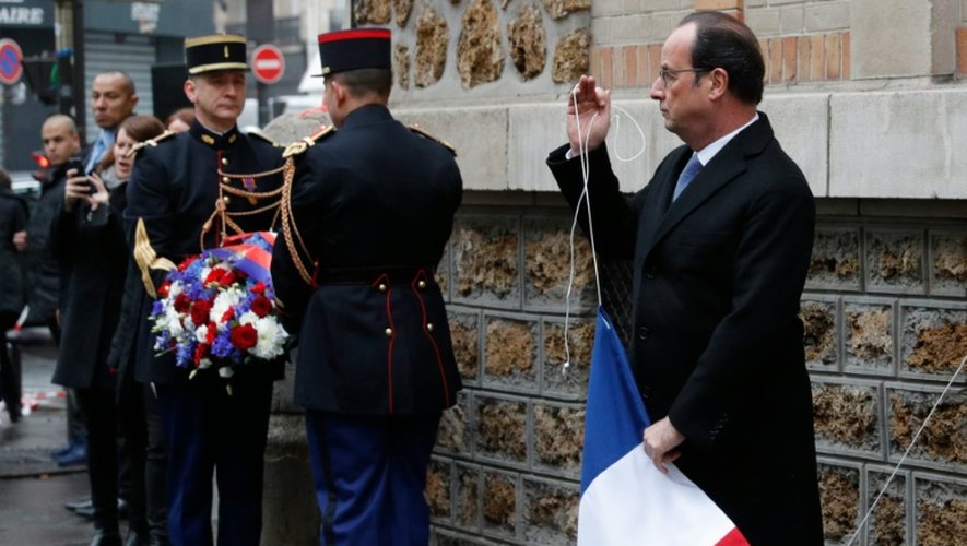 Le président Hollande tient le drapeau français après avoir dévoilé la plaque commémorative devant La Belle Equipe, le 13 novembre 2016, dans le cadre des cérémonies un an après les attentats