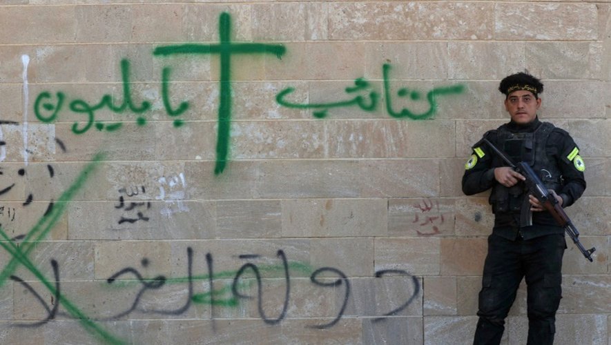 Un soldat des "Brigades de Babylone" se tient près d'un mur du monastère syriaque catholique de Mar Behnam couvert de graffitis laissés par les jihadistes de l'EI, le 22 novembre 2016 à Khidr Ilyas, en Irak