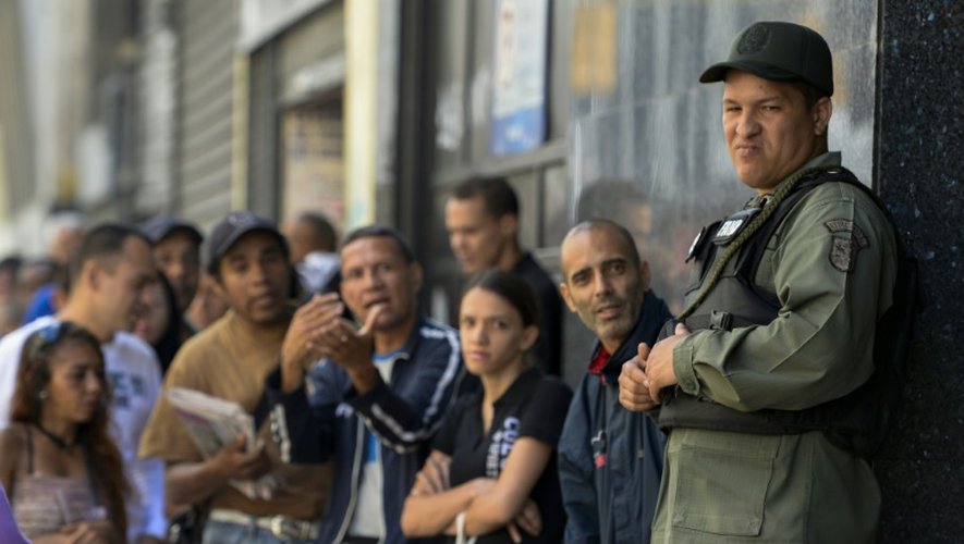 Un militaire vénézuélien surveille ceux qui font la queue devant la banque centrale de Caracas pour échanger leurs billets de 100 bolivars, le 16 décembre 2016