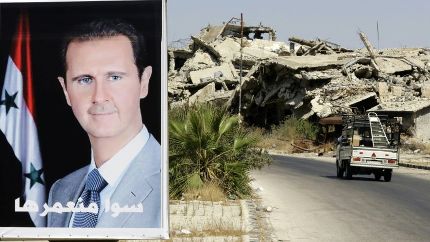 Un véhicule passe à côté d'une affiche de Bachar al-Assad et des bâtiment détruits du quartier Jouret al-Shiah à Homs le 19 septembre 2016