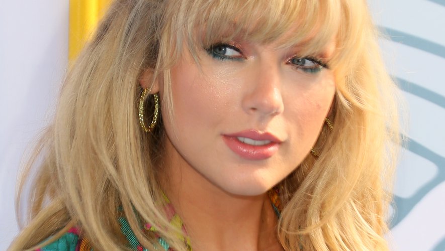 Taylor Swift a choisi un coiffé décoiffé à frange. Elle associe à cette coiffure un trait d'eyeliner coloré et un peu de gloss.