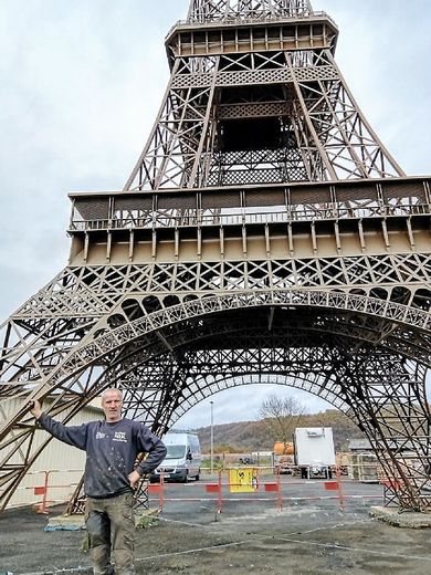 Alain Lacombe au pied de « sa » tour Eiffel de 28 mètres et 10 tonnes, une magnifique et saisissante reproduction à l’identique de l’original, à l’échelle 1/15e.