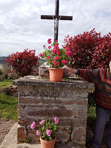 Deux habitants du hameau installent leurs pots fleuris devant la croix, en attendant de pouvoir semer des graines de fleurs au pied du socle, comme ils ont l’habitude de le faire.