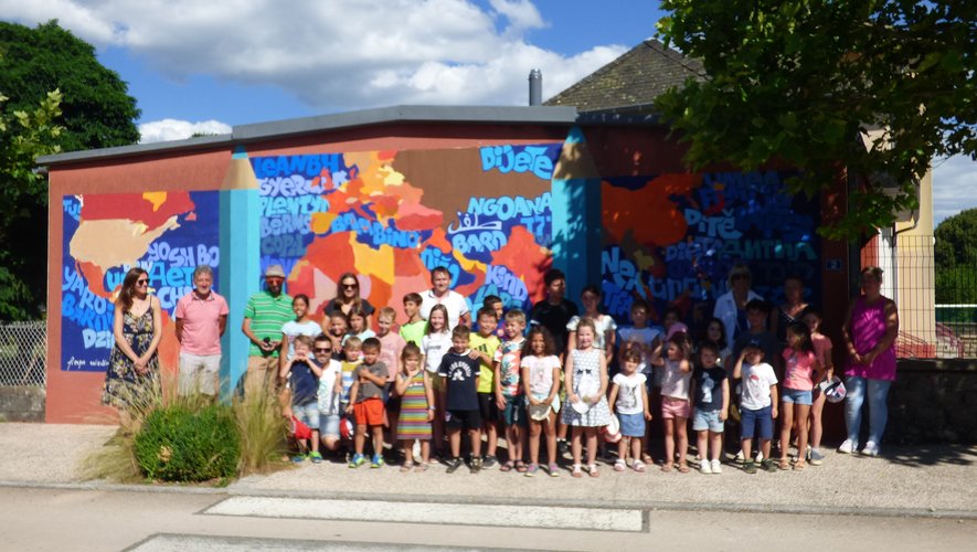 Le groupe d’enfants, l’artiste et les intervenants devant la fresque du mur de l’école.