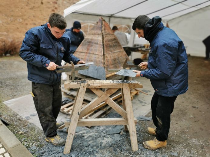 Le métier de couvreur est présenté aux visiteurs. Ces deux jeunes aspirants couvrent la maquette d'une flèche avec de l'ardoise.